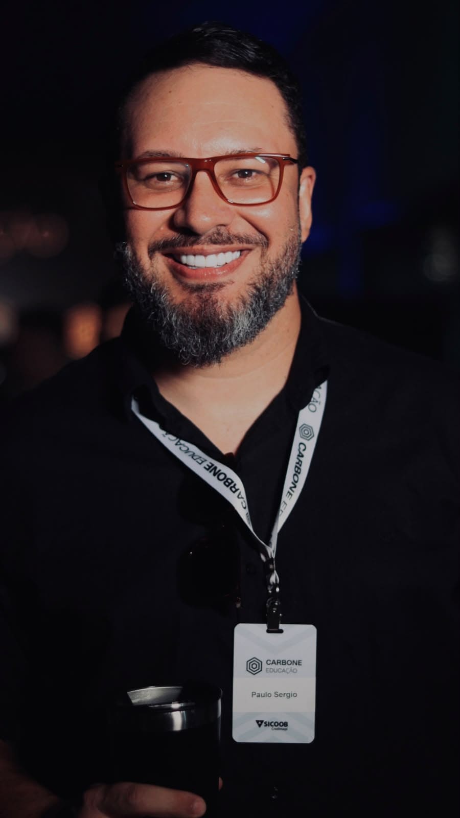 Paulo Sérgio Dantas sorrindo, de óculos e camisa preta, em um evento